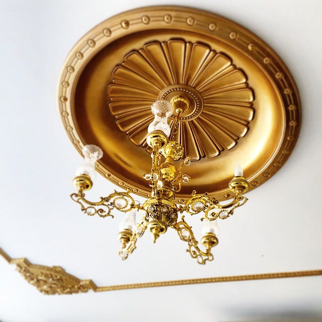 Roson din poliuretan P9106 auriu montat pe un tavan alb cu candelabru clasic într-un living de vilă.