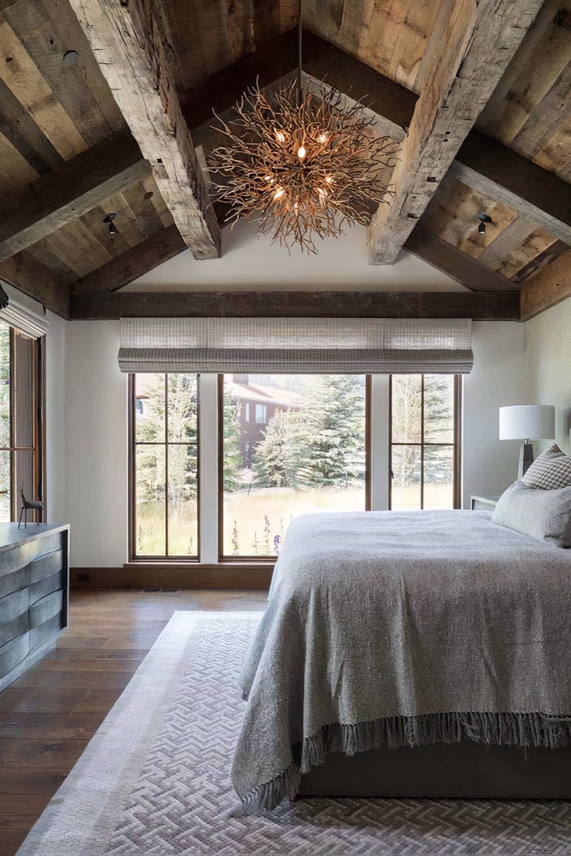 Dormitor rustic cu tavan înalt decorat cu grinzi din poliuretan, candelabru din ramuri și fereastră mare.