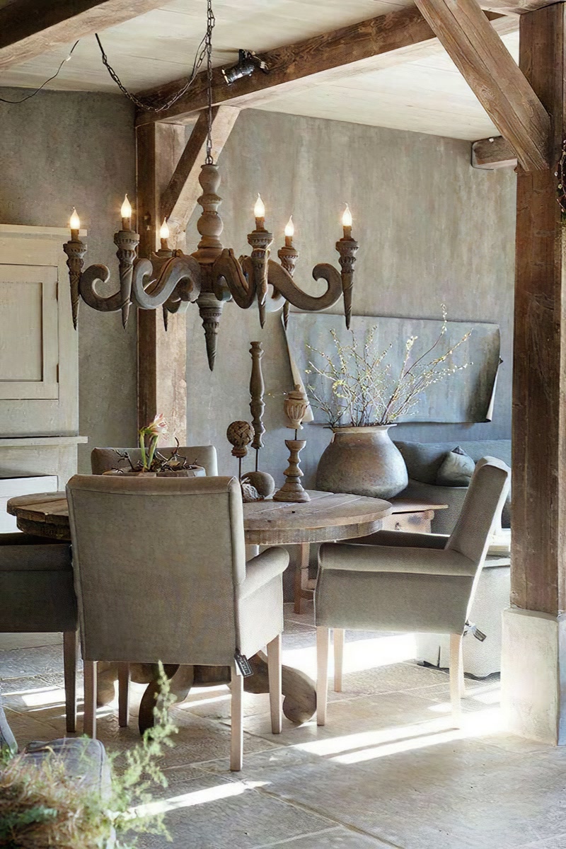 Sufragerie rustică cu masă rotundă din lemn, candelabru decorativ și grinzi din poliuretan imitație lemn pe tavan.