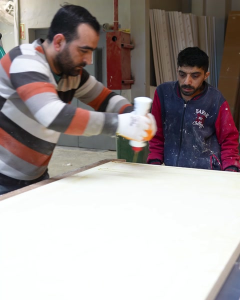 Doi muncitori aplică adeziv pe placa pentru masă