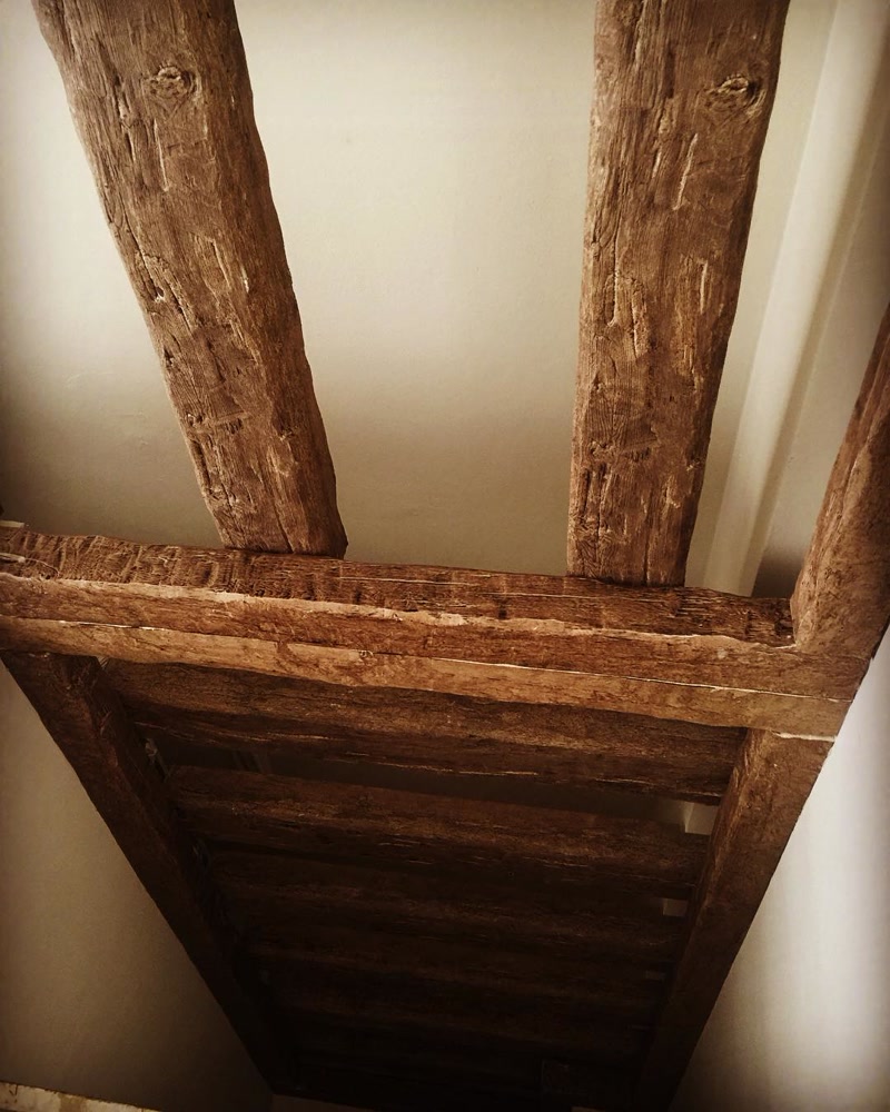 Grinzi Decorative din Poliuretan Stil Rustic Tavan Grinzile din poliuretan cu aspect de lemn rustic sunt elemente decorative ușoare, folosite pentru a crea o atmosferă primitoare în living sau zona de dining. Când ne-am dorit să aducem un aer cald și autentic în casa noastră, am ales această structură pe tavan pentru a transforma un spațiu simplu într-un loc confortabil de adunare pentru întreaga familie. Materialul are o densitate optimă de 150-220 kg/m³ (țintă ~160 kg/m³), ceea ce oferă o rezistență excelentă la impact, fără a îngreuna structura de rezistență a plafonului. Se îmbină perfect cu nuanțele neutre ale pereților, adăugând profunzime vizuală și un caracter cald încăperii.
Pentru amenajarea tavanului, am combinat profilul principal de grindă P1981B cu profilul secundar P1981C, ambele având un finisaj maro închis ce imită fidel textura lemnului cioplit manual. Această combinație de profile transversale creează o rețea vizuală echilibrată, oferind iluzia unui tavan înalt și bine structurat. Spre deosebire de grinzi din lemn masiv, poliuretanul prezintă un coeficient de absorbție a apei de sub 1%, ceea ce face ca aceste elemente să nu se deformeze și să nu crape în timp din cauza fluctuațiilor de umiditate din casă.
Utilizarea zilnică a acestui spațiu devine mult mai plăcută datorită ambianței create de lumina caldă care se reflectă pe suprafața structurată a grinzilor. Poliuretanul rezistă excelent la temperaturi cuprinse între -100 °C / +80 °C, fiind un material ideal pentru orice zonă a locuinței, inclusiv lângă bucătării sau spații bine iluminate natural. Întreținerea este extrem de simplă, fiind suficientă ștergerea periodică de praf cu o lavetă moale, fără a fi nevoie de tratamente speciale cu lacuri sau uleiuri protectoare ca în cazul lemnului natural.
Rezultatul final al acestei amenajări cu grinzi decorative din poliuretan oferă familiei noastre un spațiu plin de căldură și personalitate, perfect pentru serile petrecute împreună. Montajul simplu prin lipire directă a permis finalizarea rapidă a proiectului fără șantiere lungi sau praf excesiv. Pentru proprietarii de case care își doresc un decor rustic autentic fără complicații tehnice, această soluție decorativă reprezintă alegerea practică și durabilă pentru un cămin primitor.
