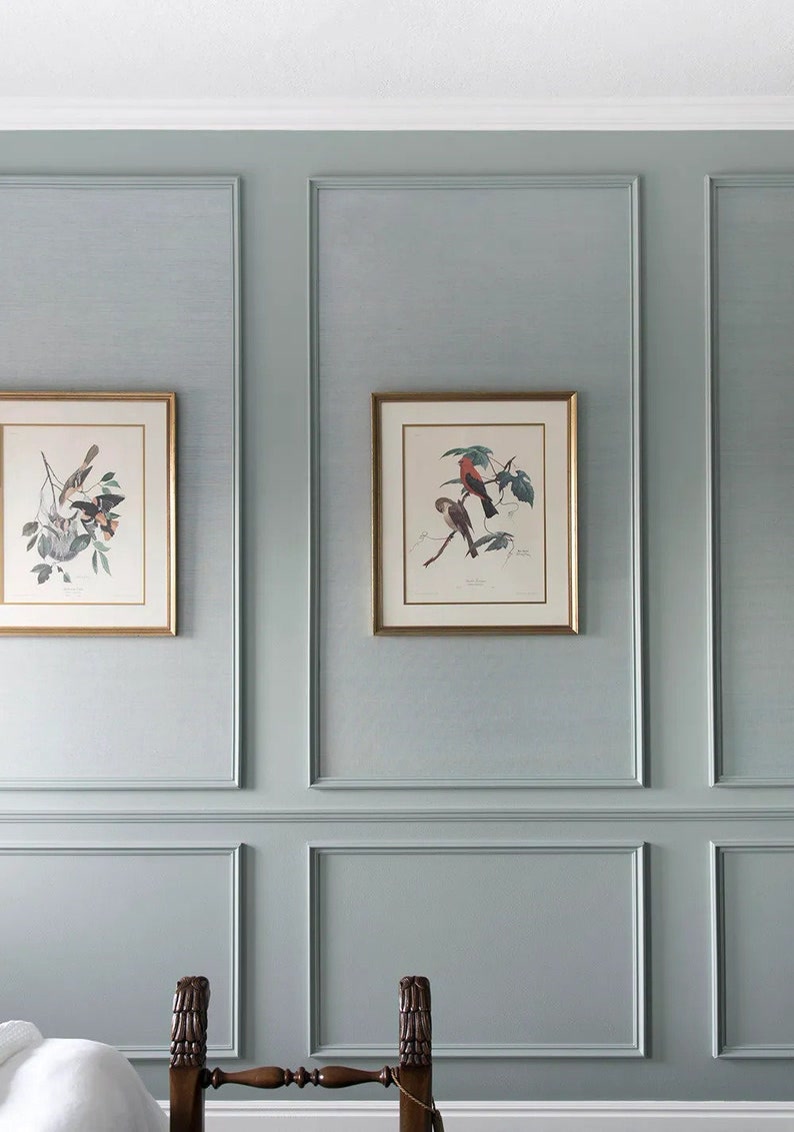 Profil Poliuretan Decorativ pentru Perete Dormitor Decorarea peretelui cu profile din poliuretan reprezintă o tehnică eficientă de finisaj interior care adaugă relief și structură suprafețelor plane. În dormitorul nostru, am ales o nuanță liniștitoare de verde salvie care îmbracă întreaga suprafață a peretelui, oferind un fundal relaxant pentru fiecare dimineață. Această culoare pastelată interacționează într-un mod plăcut cu lumina naturală, creând o atmosferă primitoare și caldă în încăpere. În combinație cu un pat din lemn masiv de culoare închisă, spațiul capătă un aer reconfortant și echilibrat, ideal pentru odihnă.
Pentru realizarea casetelor decorative de pe perete, am utilizat baghete din poliuretan de înaltă densitate, având o valoare de aproximativ 150-220 kg/m³ (țintă ~160 kg/m³). Aceste elemente arhitecturale prezintă o rezistență excelentă la impact și o absorbție de apă de sub 1%, fiind perfecte pentru utilizare pe termen lung în orice zonă a casei. Structura peretelui a fost împărțită pe orizontală și verticală folosind modelele P85016 și P85403. Materialul rezistă la variații de temperatură între -100 °C / +80 °C, garantând că stabilitatea dimensională rămâne intactă în timp, fără risc de fisurare la îmbinări.
Integrarea tablourilor cu ilustrații botanice și păsări în interiorul casetelor superioare aduce o notă personală întregului ansamblu. Ramele subțiri cu finisaj auriu creează un contrast cald cu tonul rece al peretelui verde salvie. După montajul profilelor, îmbinările au fost finisate prin șlefuire ușoară cu hârtie abrazivă de granulație 220 și acoperite cu 2 straturi de vopsea lavabilă pe bază de apă. Vopsirea baghetelor în aceeași culoare cu peretele oferă un efect vizual unitar, permițând luminii să evidențieze discret umbrele și volumetria finisajului.
O astfel de amenajare demonstrează cum detaliile geometrice pot schimba complet percepția asupra unui dormitor obișnuit. Casetele verticale alungesc optic peretele spre tavan, oferind senzația unui spațiu mai înalt și mai aerisit. Fiecare moment petrecut în acest dormitor reflectă atenția la detalii și dorința de a crea un cămin armonios. Pentru oricine își dorește o transformare curată și de durată, utilizarea acestor profile decorative rămâne o opțiune practică și estetică.
